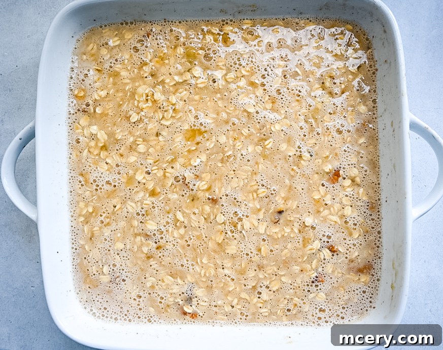 Delicious and Nutritious Banana Bread Baked Oatmeal 7 A person holding a spoon, scooping out a piece of Banana Bread Baked Oatmeal from the baking dish, showing its soft texture.