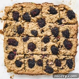 Blackberry Banana Bliss Bars 5 A large tray of baked Blackberry Banana Bread Bars topped with blackberries. The squares are slightly browned, crumbly, and arranged neatly in a grid. The juicy berries are scattered across the surface, adding a burst of dark color.