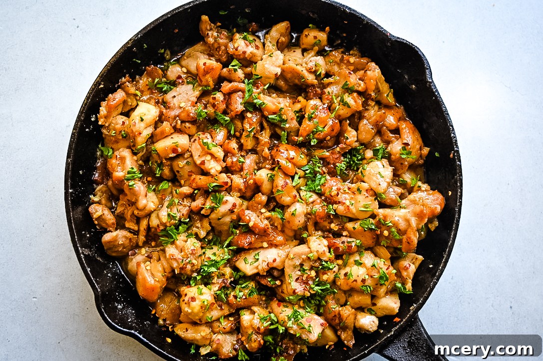 Sticky Sweet Garlic Chicken Bites 5 Close-up of a skillet filled with glossy, dark honey garlic chicken bites, some slightly charred, indicating a deep caramelized flavor.