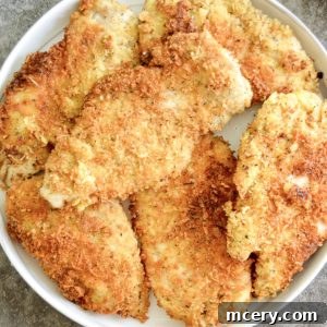 Parmesan Crusted Gluten-Free Chicken 8 A plate filled with crispy, golden-brown Gluten-Free Parmesan Chicken Cutlets is displayed. The chicken pieces are arranged neatly, highlighting their crunchy texture. The background is a simple gray surface.