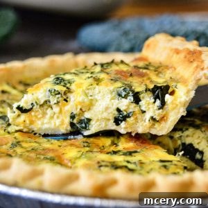 A close-up of a freshly baked Kale, Broccoli, And Cheddar Quiche with a golden, flaky crust. A slice is being lifted, revealing a filling of eggs, cheese, and greens. The quiche sits in a foil pie dish, and a leafy vegetable is blurred in the background.