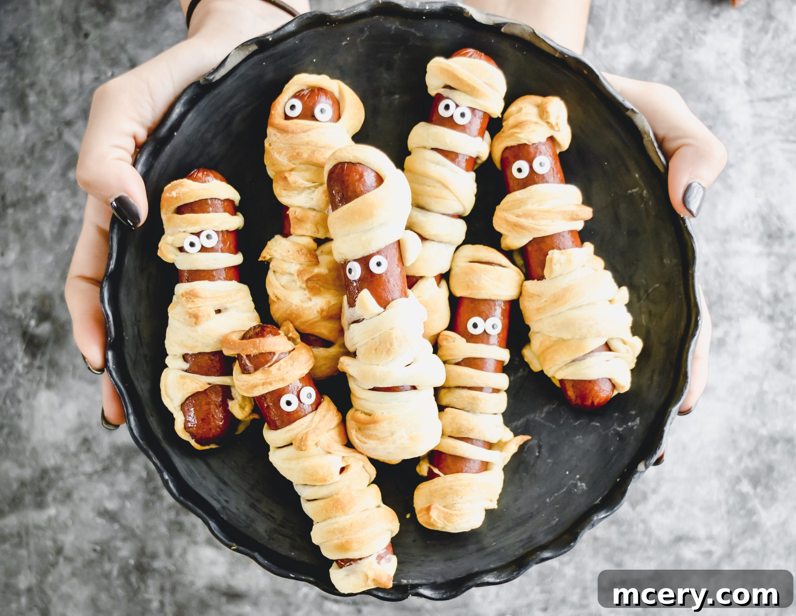 Halloweenie Wraps 2 Mummy Dogs arranged on a plate, ready to be served. Hot dogs are wrapped in crescent dough to resemble mummies, with small gaps for eyes, creating a festive Halloween appetizer.