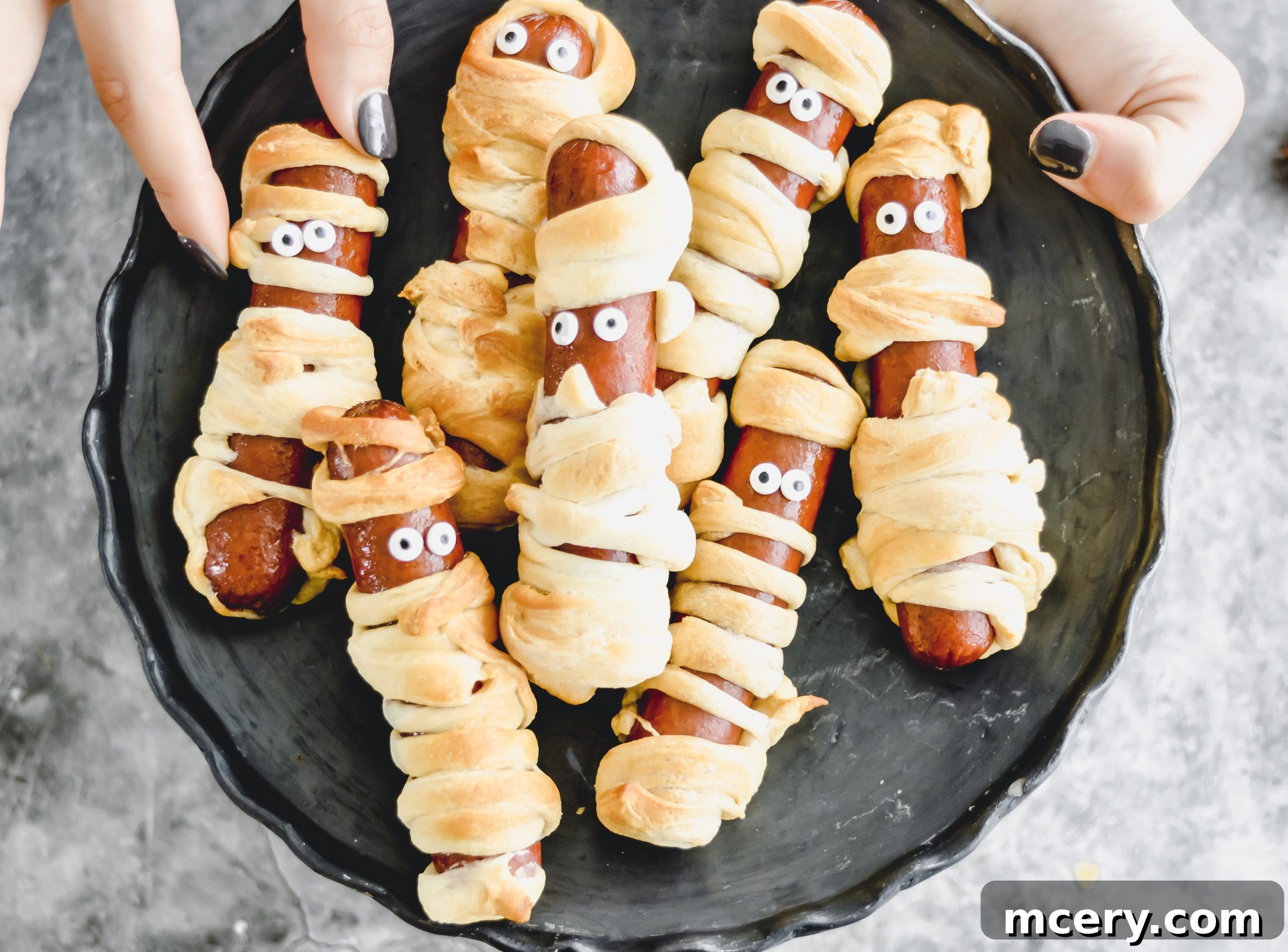 Halloweenie Wraps 5 A hot dog partially wrapped in strips of crescent roll dough, demonstrating the technique for creating the mummy-like appearance before baking. The dough is strategically placed to mimic bandages.