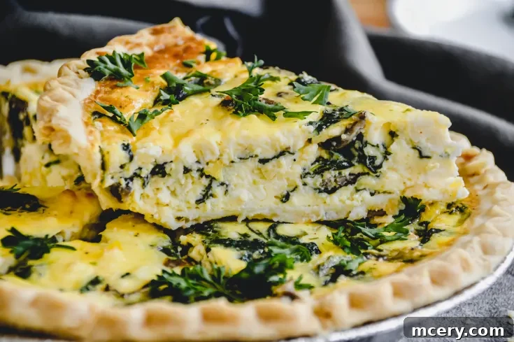 Close-up of a Spinach, Mushroom, and Feta Quiche with a flaky crust. The quiche is topped with fresh parsley and features a creamy, textured filling with visible spinach leaves. A slice is cut and slightly lifted from the whole quiche.