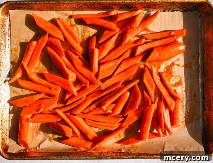 Golden Maple Glazed Carrots 7 Seasoned carrots spread in a single layer on a parchment-lined baking sheet.