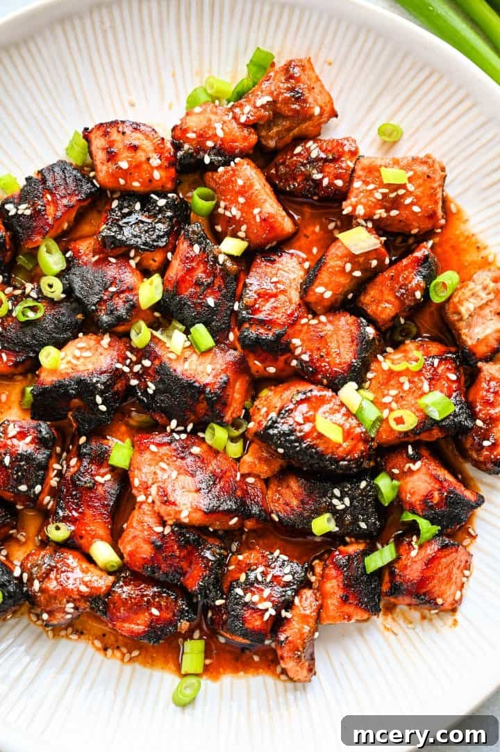 Honey Glazed Salmon Bites with Sesame Ginger and Smoked Paprika 2 Beautifully caramelized honey baked salmon bites on a white plate, garnished with green onions and sesame seeds, ready to be served.