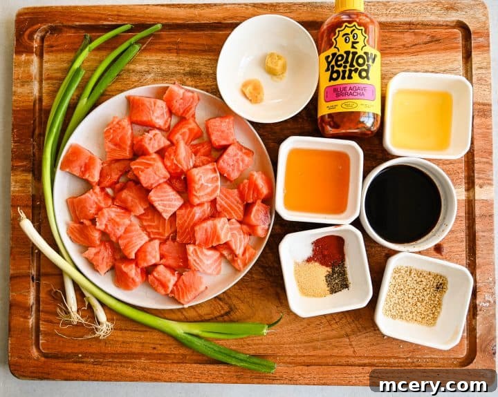 Honey Glazed Salmon Bites with Sesame Ginger and Smoked Paprika 3 Overhead view of cubed salmon and small bowls of sesame oil, honey, soy sauce, garlic, ginger, and seasonings arranged on a wooden board for Honey Baked Salmon Bites.