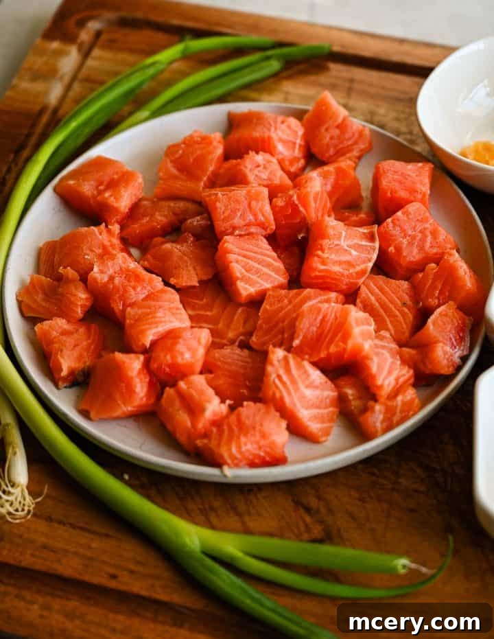 Honey Glazed Salmon Bites with Sesame Ginger and Smoked Paprika 4 Raw cubed salmon in a bowl with sliced green onions and small bowls of honey, soy sauce, sesame oil, garlic, ginger, and spices arranged on a wooden board.