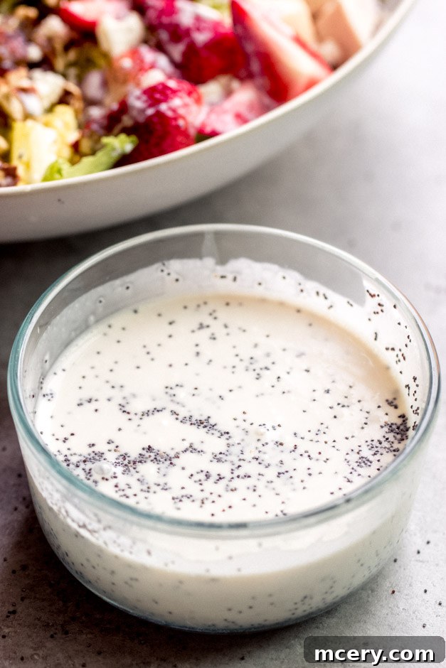 Fresh Homemade Poppy Seed Dressing 5 A hand drizzling homemade poppy seed dressing over a fresh green salad with berries and nuts.
