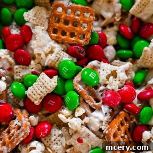 Close-up of Reindeer Crunch Snack Mix with Chex cereal, pretzels, popcorn, white chocolate, crushed peppermint, and red and green Christmas M&M’s.