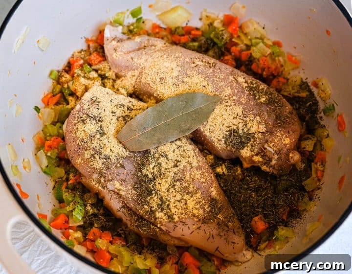 Soul Soothing Chicken Noodle Soup 6 Raw chicken pieces seasoned with salt and pepper, nestled amongst sautéed vegetables in a large pot, ready for the next stage of soup preparation.