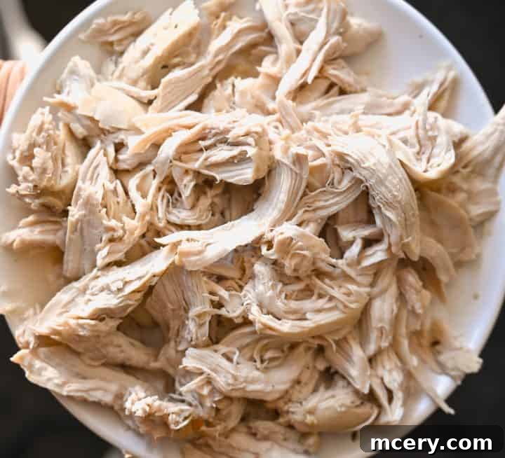 Soul Soothing Chicken Noodle Soup 8 Cooked chicken being shredded with two forks on a cutting board, ready to be returned to the soup.