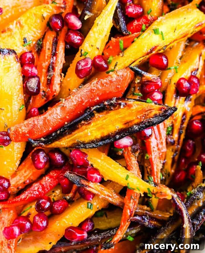 Honey butter roasted rainbow carrots with golden edges, pomegranate seeds, and fresh chives served in a white bowl.