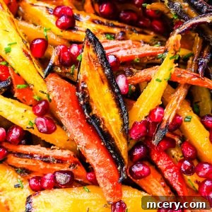 Honey butter roasted rainbow carrots with golden edges, pomegranate seeds, and fresh chives served in a white bowl.