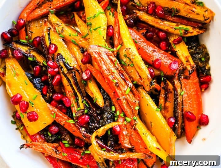 Honey butter roasted rainbow carrots with golden edges, pomegranate seeds, and fresh chives served in a white bowl.