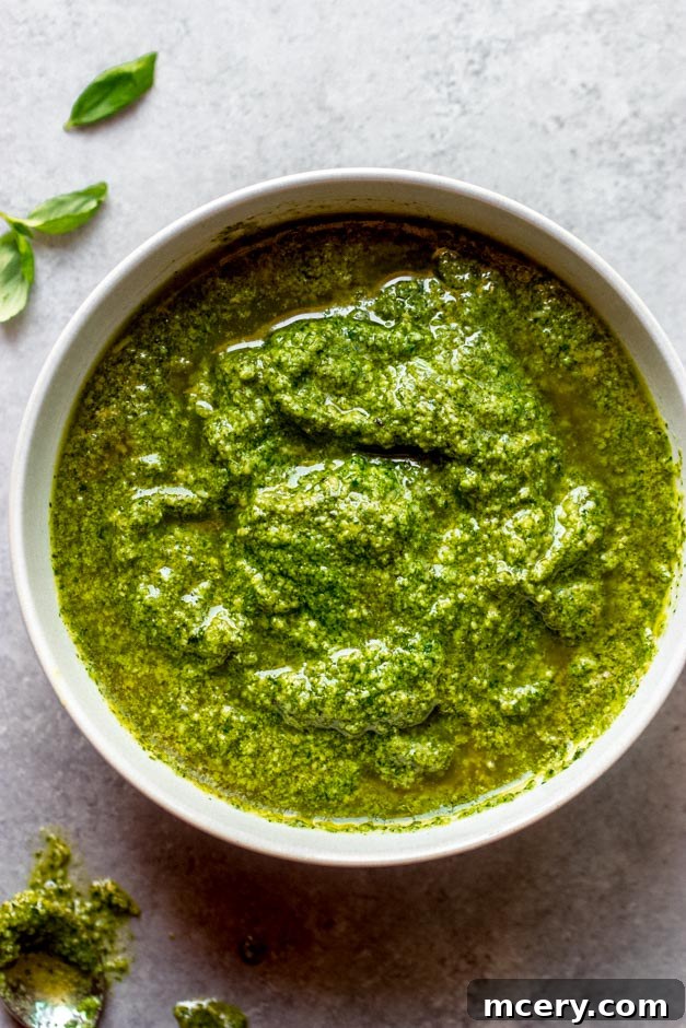 A beautifully presented bowl filled with vibrant green homemade basil pesto, garnished with fresh basil leaves and toasted pine nuts, set on a rustic wooden surface, ready to be enjoyed.