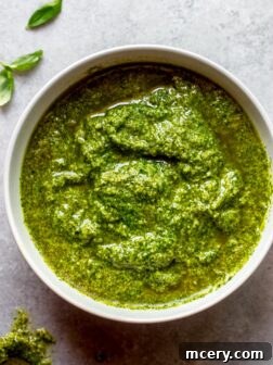 Homemade basil pesto in a serving bowl, garnished with fresh basil leaves and pine nuts.