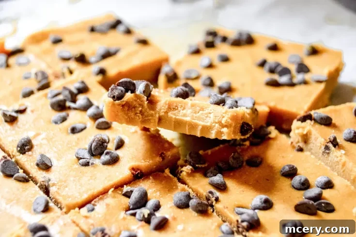Close-up of sliced Pumpkin Chocolate Chip Fudge topped with chocolate chips. A piece is held above the rest, showing its creamy texture and chocolate chip topping. The fudge is arranged on a white surface.