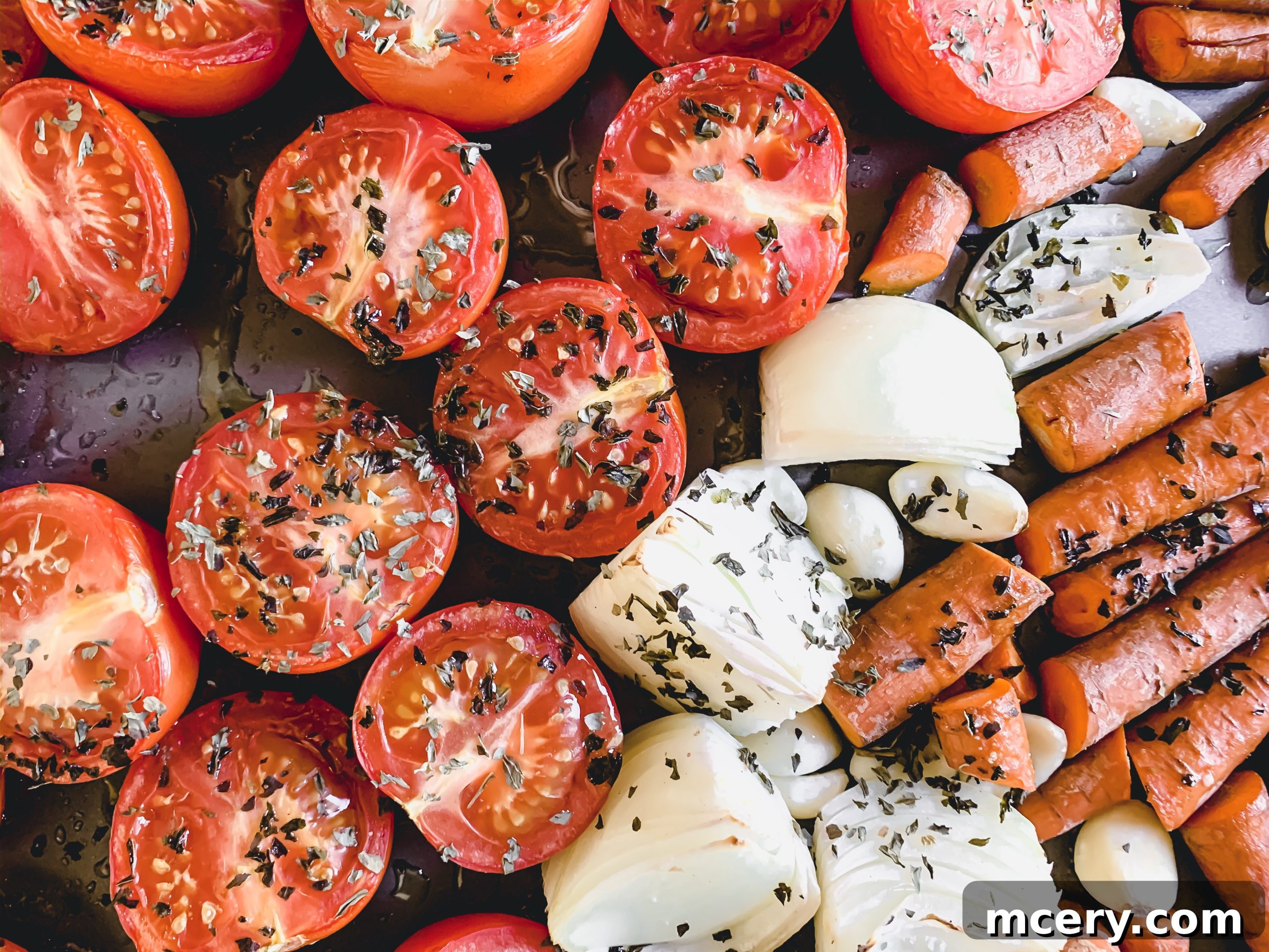 A close-up view of vibrant, freshly roasted tomatoes, carrots, onions, and garlic spread on a baking sheet, showcasing their beautiful caramelization.