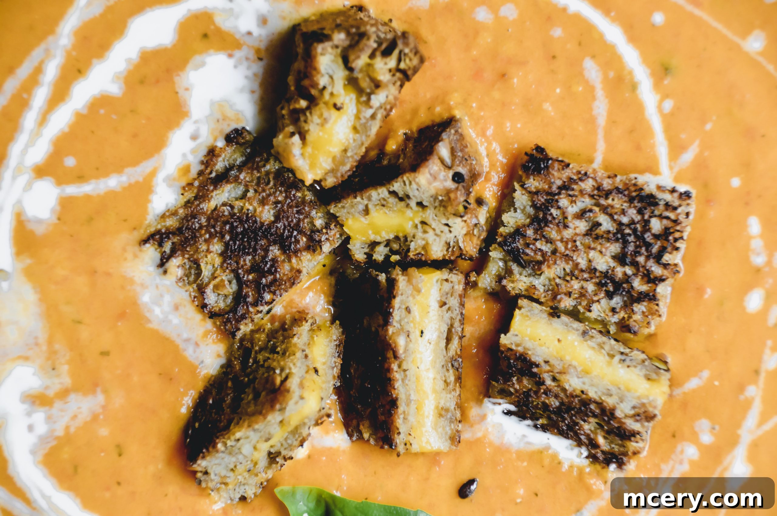 A bowl of creamy Roasted Tomato Soup garnished with fresh basil, accompanied by a side plate of golden, crispy mini grilled cheese croutons.