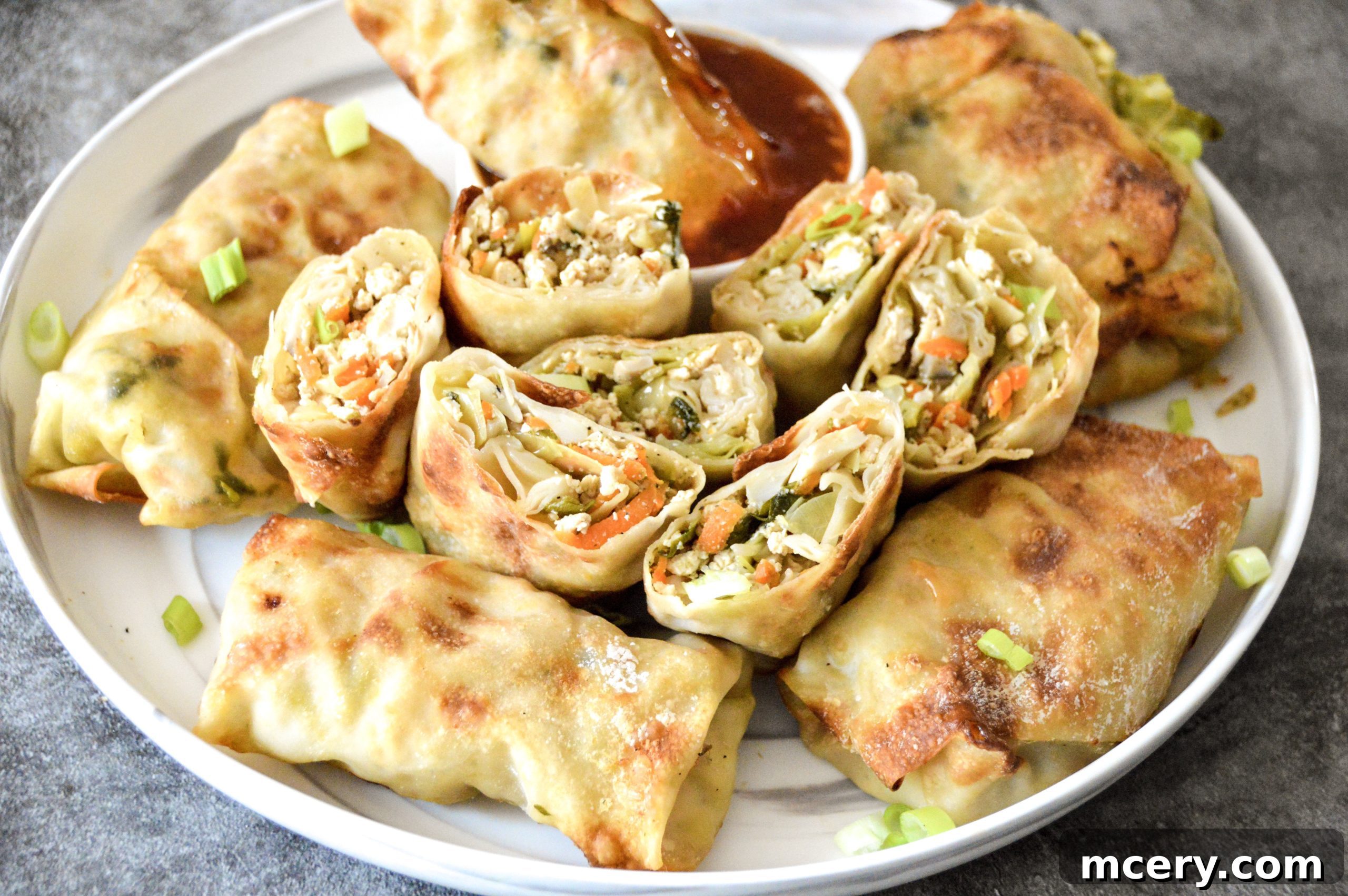 Golden Crispy Air Fryer Veggie Tofu Rolls 4 A platter of freshly air-fried egg rolls, some whole and some cut to reveal the vibrant vegetable and tofu filling.