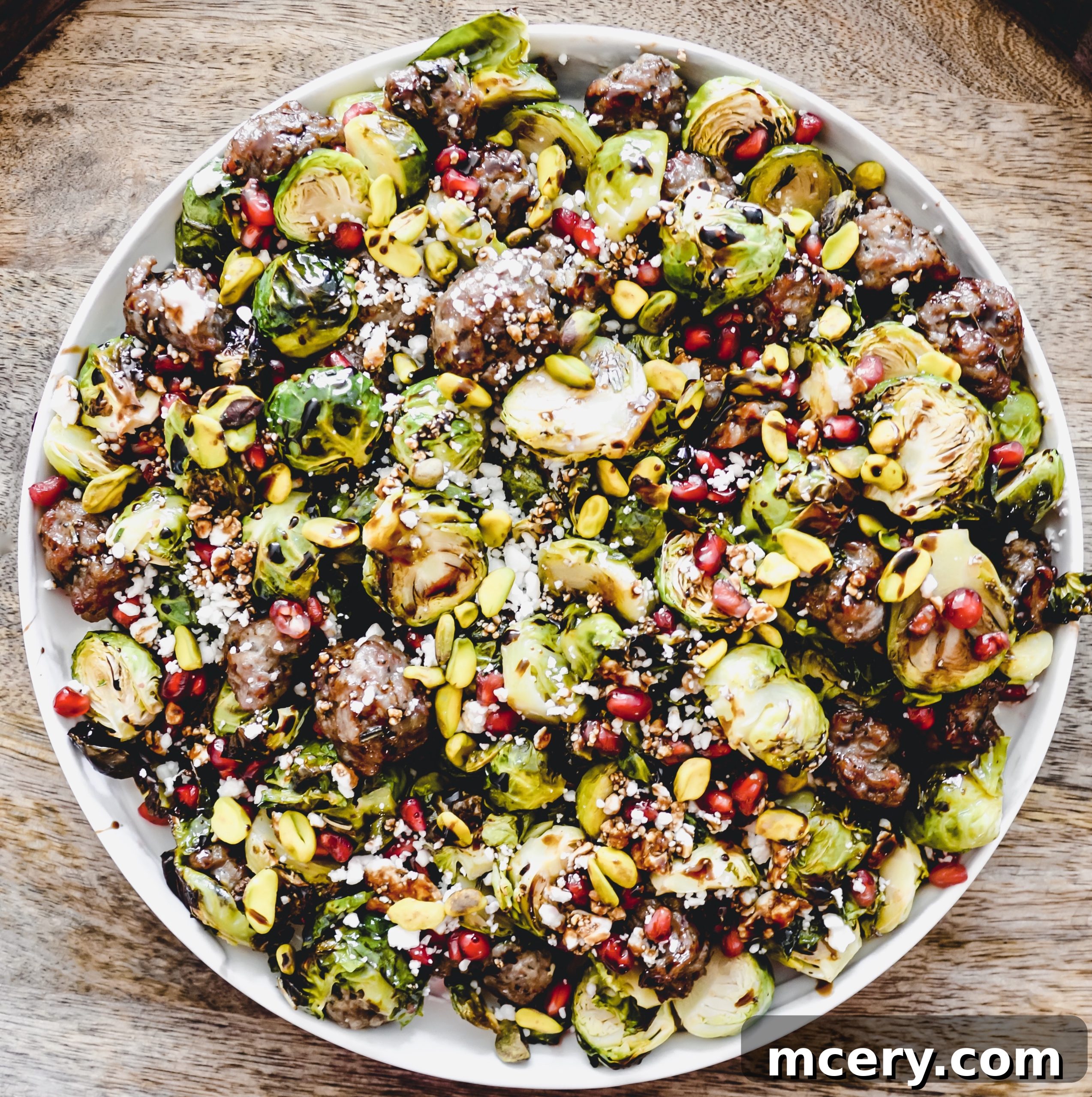 Close-up of the roasted Brussels sprouts and sausage mixture, garnished with fresh pomegranate seeds and crumbled feta cheese, ready for serving.