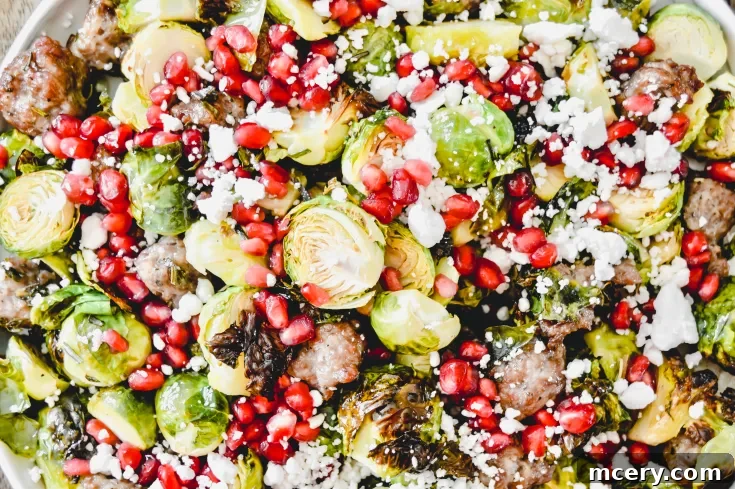 A close-up of Roasted Brussels Sprouts with Sausage, pomegranate seeds, crumbled feta cheese, and pieces of sausage. The vibrant colors and textures create a visually appealing dish.