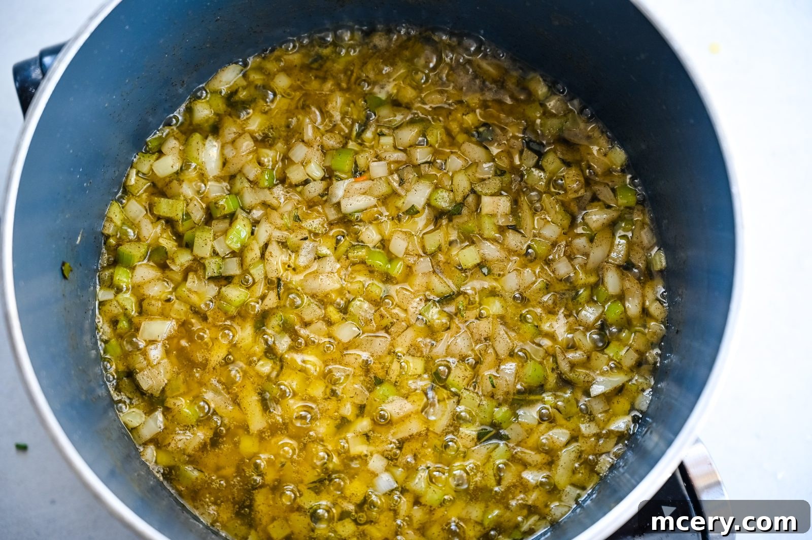 Pratik İç Harcı Tarifi: Şükran Günü Sofralarının Yıldızı 8 A pot filled with a mixture of finely chopped celery and onions simmering in butter, giving off a rich golden color. The mixture is cooking on a stovetop in preparation for making easy stuffing.