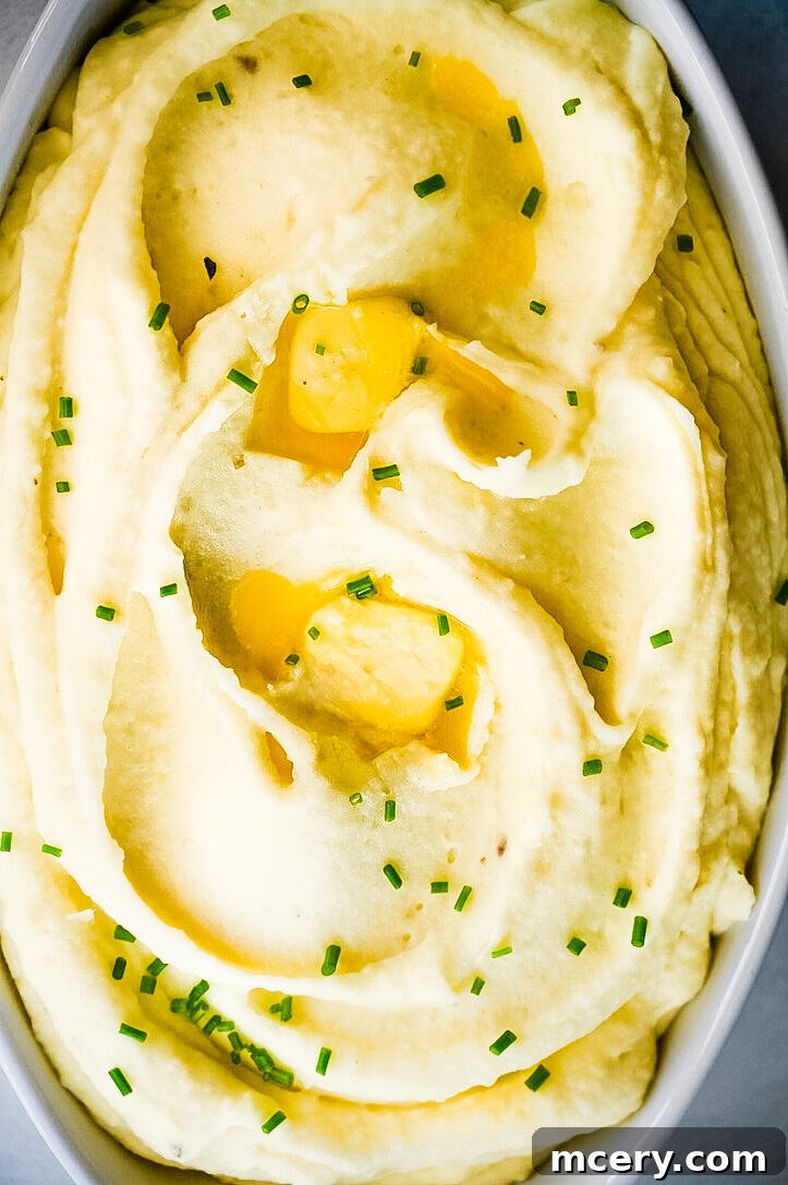 Melt-in-Your-Mouth Mashed Potatoes 2 A serving of perfectly creamy mashed potatoes in a white bowl, garnished with fresh herbs and a pat of melting butter. The texture appears smooth and inviting, hinting at the rich flavor.