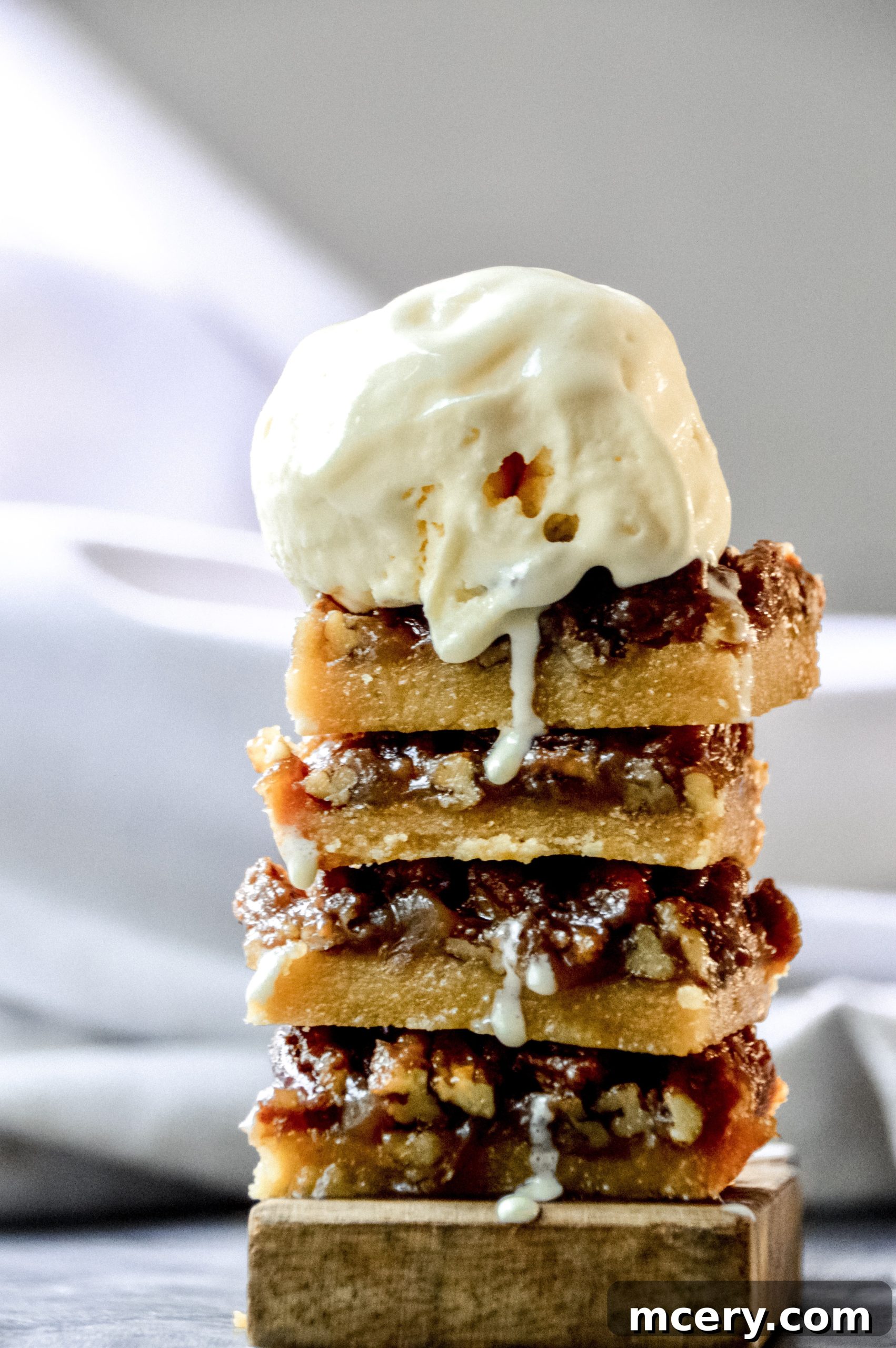 Close-up of a stack of Pecan Pie Bars, showing the gooey pecan topping and a thick, golden shortbread crust below.