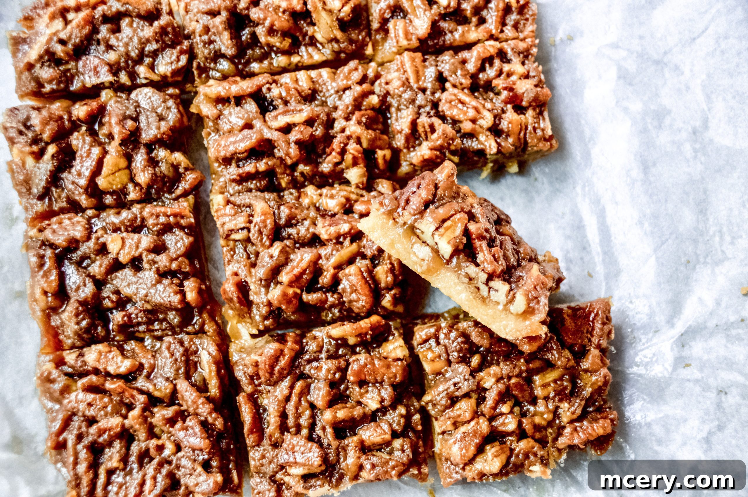A close-up of a Pecan Pie Bar on a white surface, highlighting its glistening, rich pecan topping.