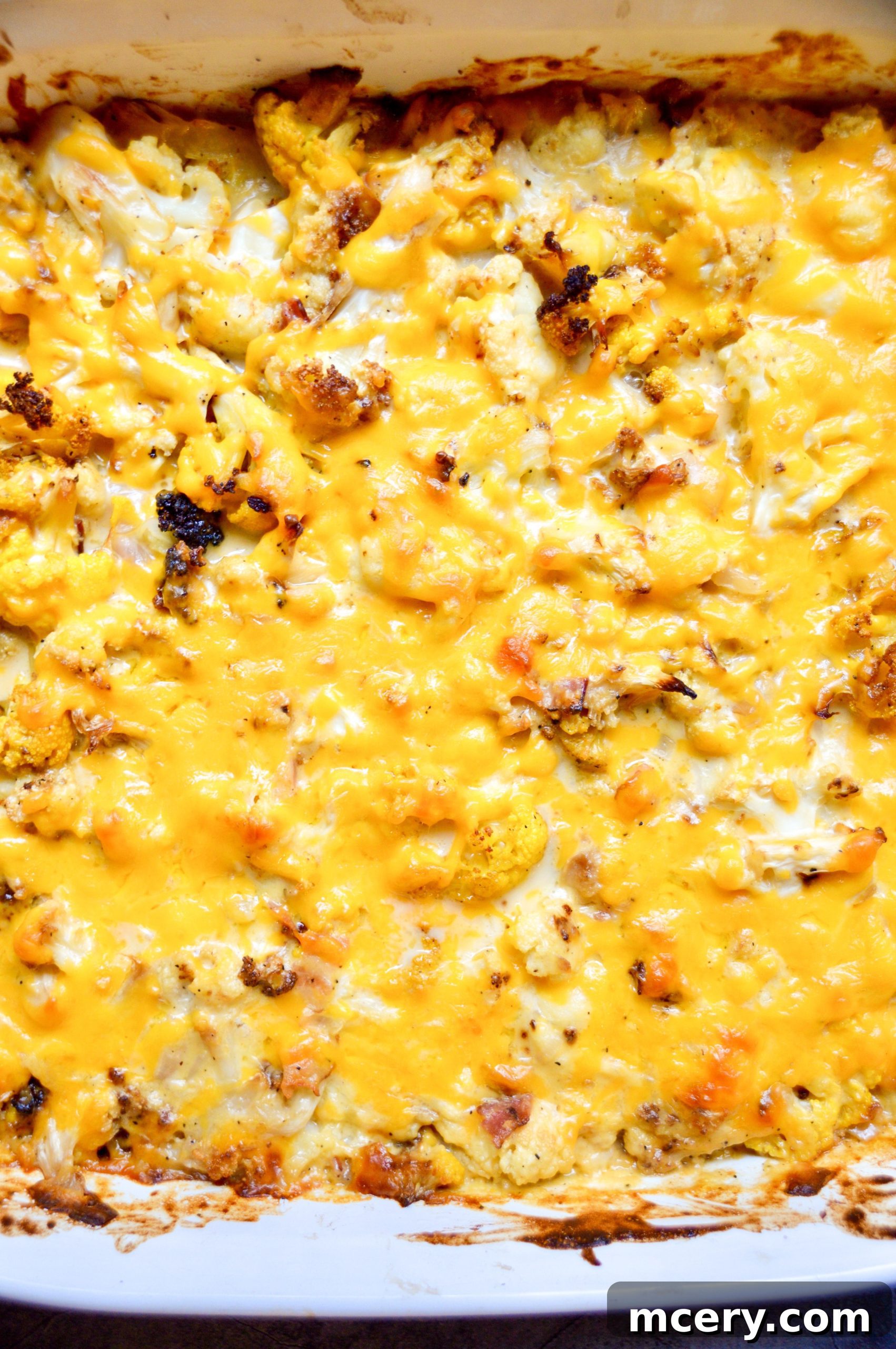 Golden Baked Cauliflower Mac & Cheese 6 A baking dish filled with cauliflower florets coated in rich cheese sauce, topped with more shredded cheese and bacon bits, ready for the oven.