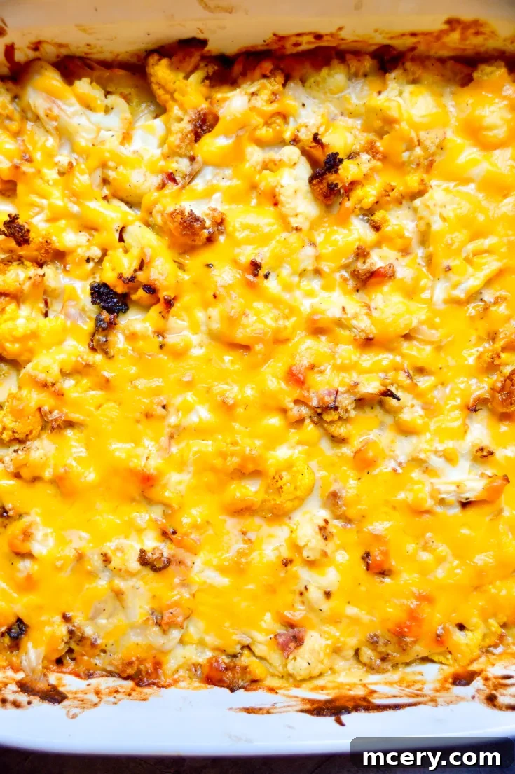 A baked casserole dish filled with golden-brown Cauliflower Mac And Cheese. The top is crisp and bubbly, with scattered bits of roasted cauliflower. The dish is on a red and white checkered cloth.