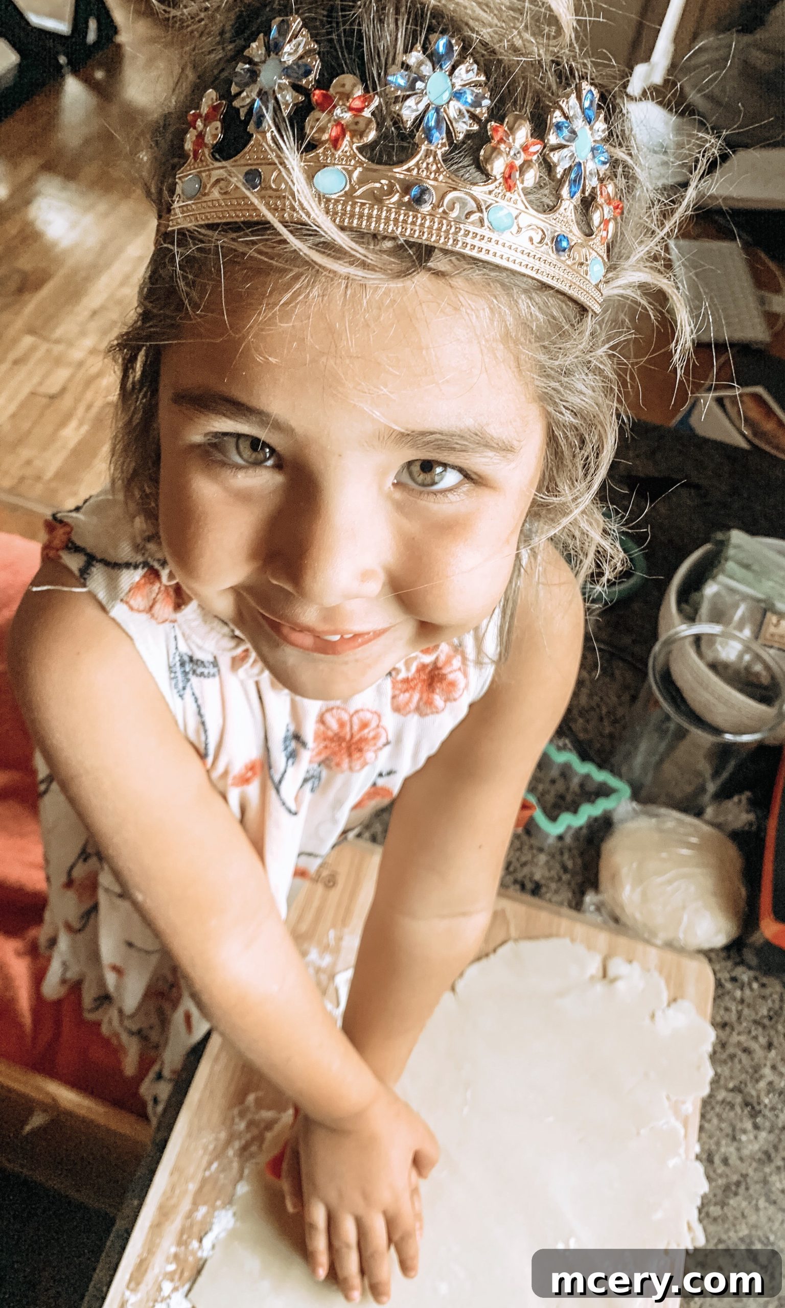 A close-up of a child's hands carefully placing cookie dough cutouts onto a baking sheet, with various festive shapes visible.