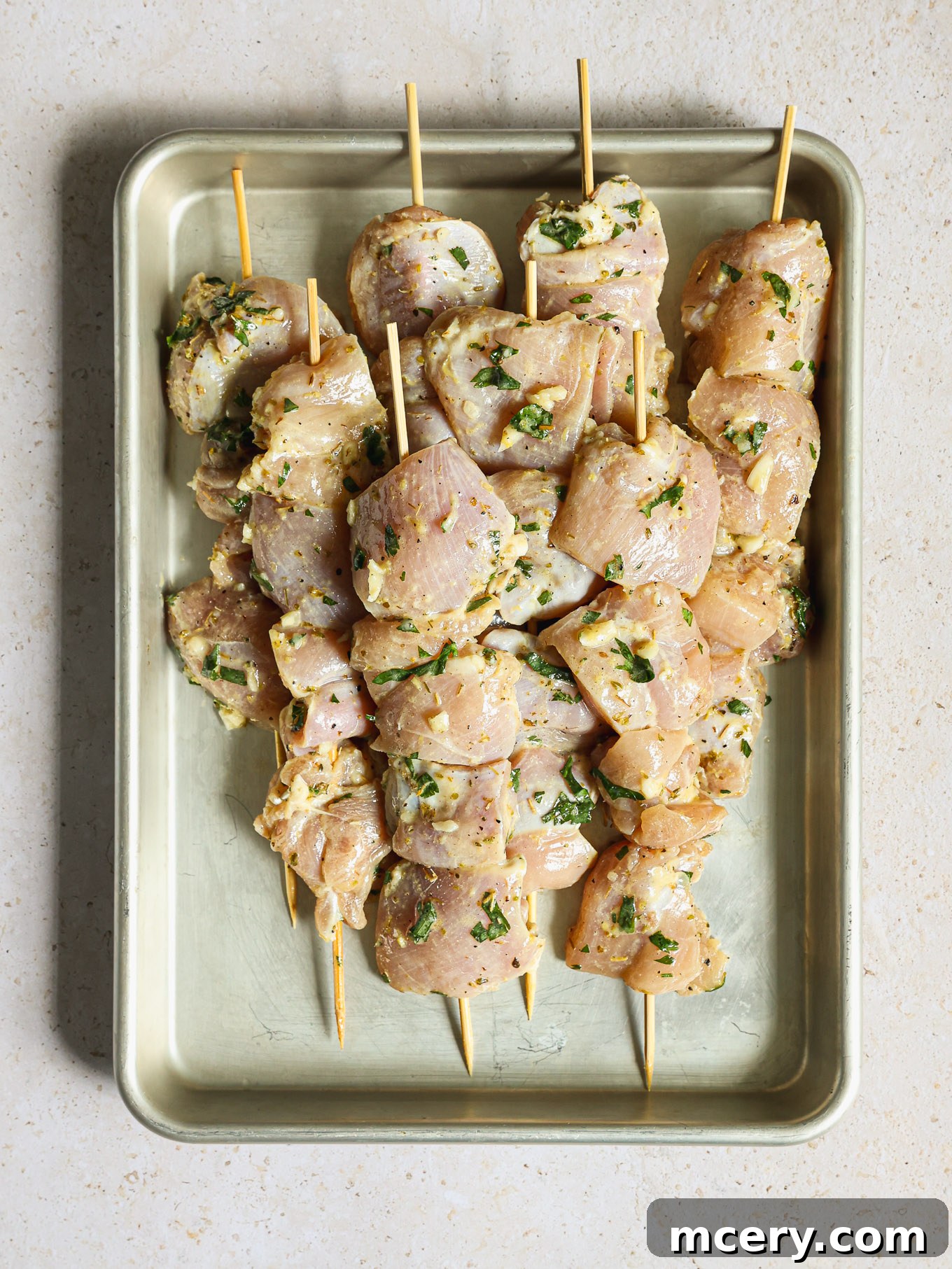 Raw marinated chicken pieces carefully threaded onto wooden skewers, ready for grilling.