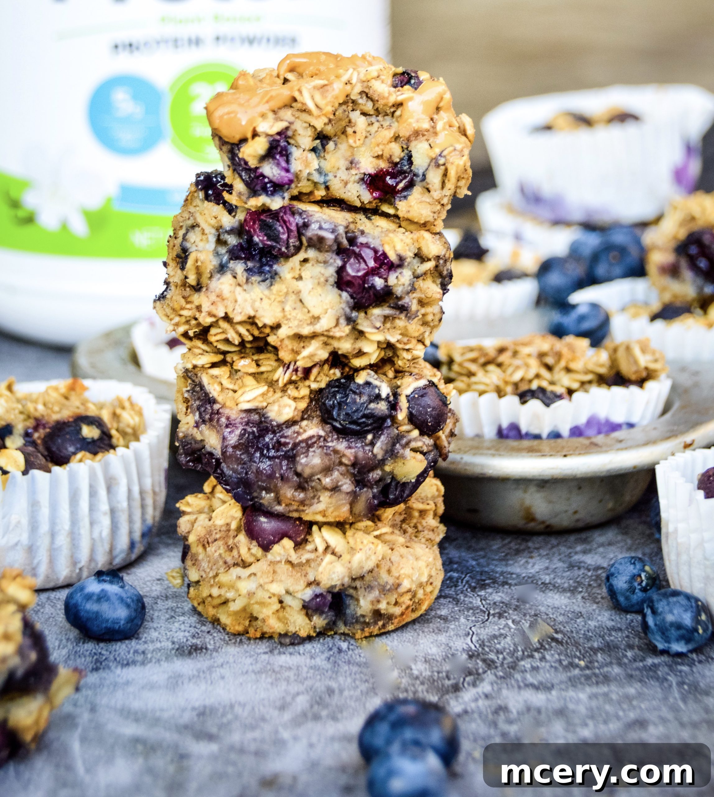 Grab-and-Go Blueberry Protein Oatmeal Cups 2 A beautifully arranged stack of Blueberry Protein Oatmeal Cups, topped with fresh blueberries and a dollop of nut butter. Additional cups are visible in the background, ready for enjoyment.