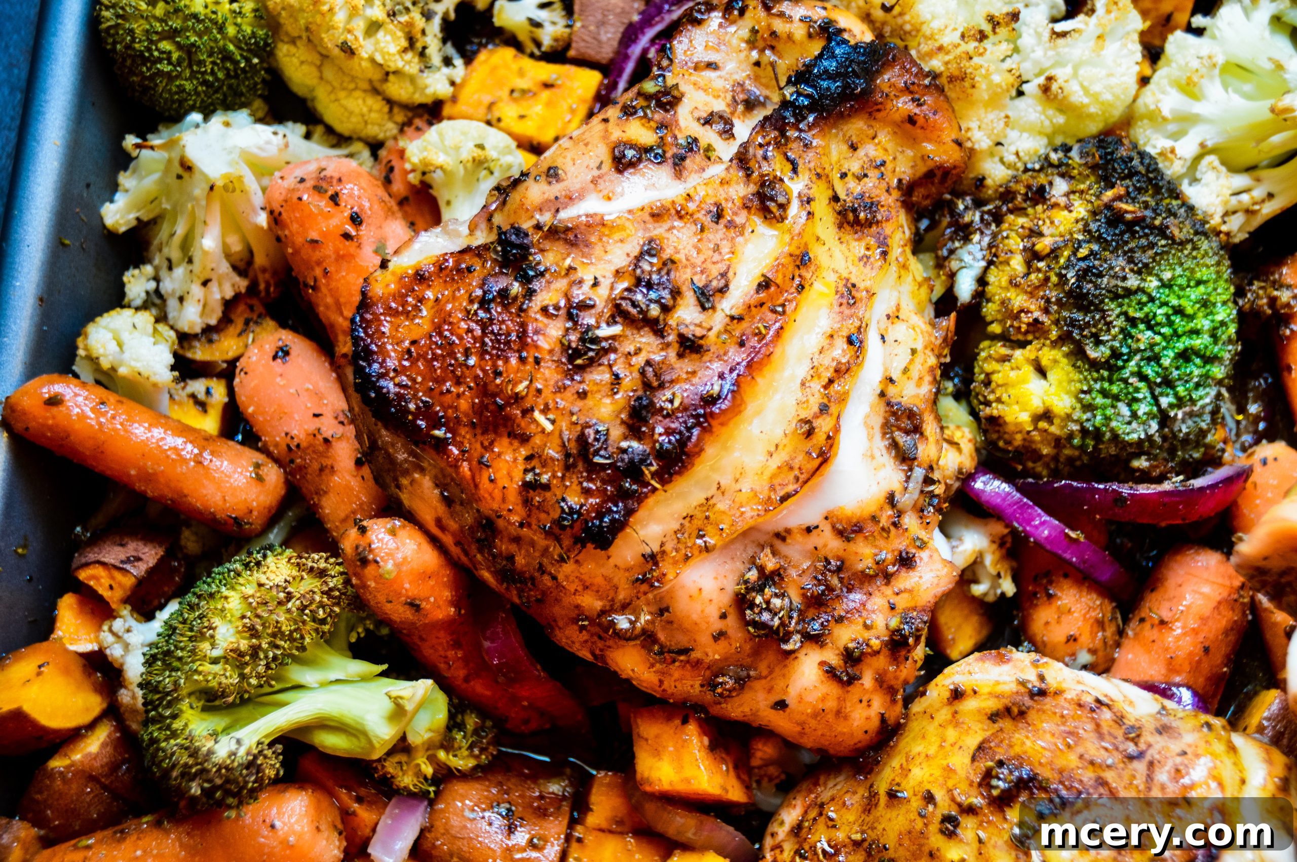 Close-up of marinated chicken thighs and chopped vegetables on a sheet pan before baking.