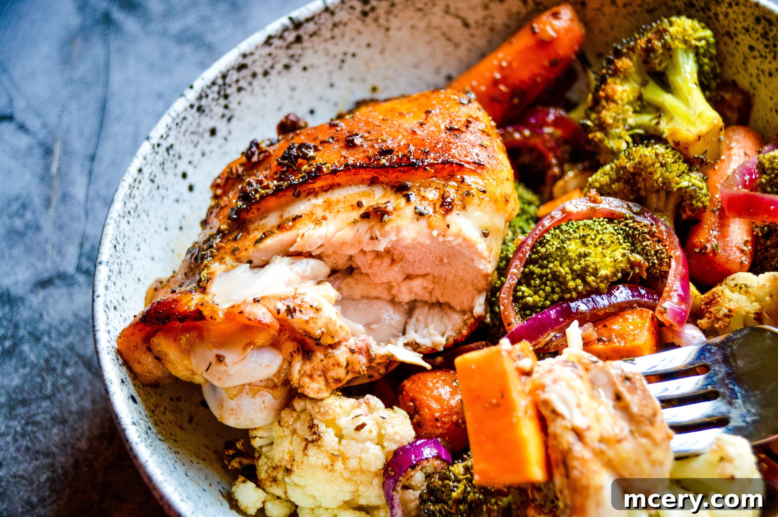 A sheet pan with raw chicken thighs coated in balsamic marinade and various vegetables, ready for the oven.