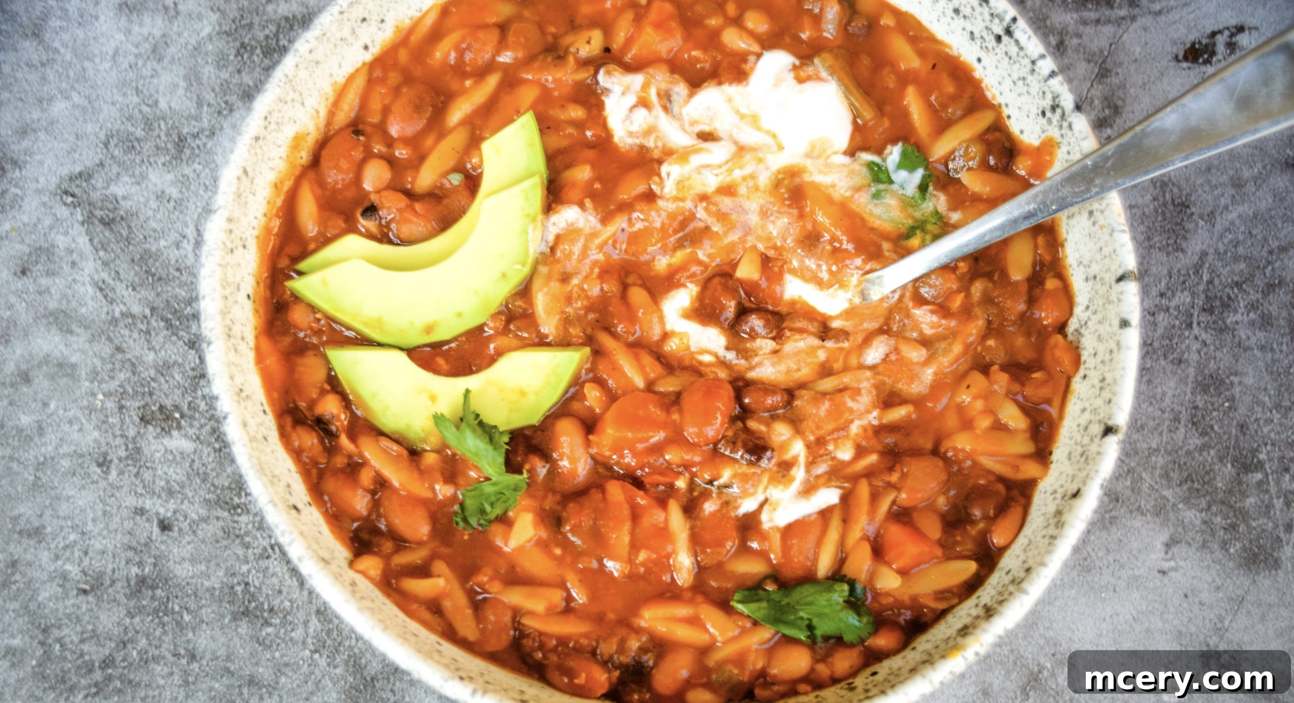 Close-up of a serving of Instant Pot Vegan 10 Bean Taco Soup, showcasing the texture of the beans and orzo in a deep red broth. The soup is presented in a white bowl with a spoon, ready to be enjoyed as a comforting and nutritious meal.