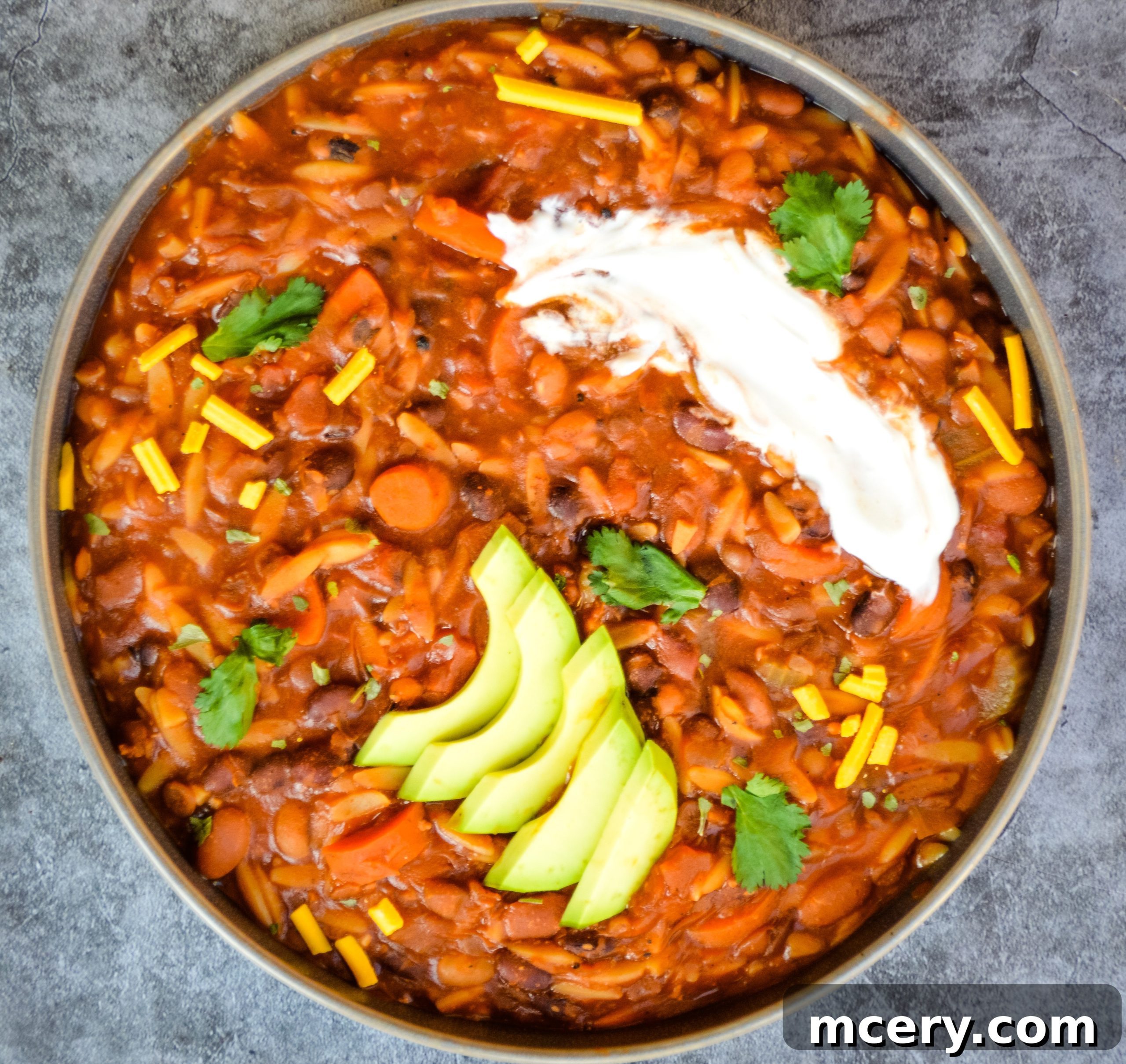 A top-down view of a generously sized bowl of Instant Pot Vegan 10 Bean Taco Soup, garnished with a sprig of fresh cilantro, a dollop of vegan sour cream, and a sprinkle of crushed tortilla chips. The inviting presentation highlights the rich colors and textures of the soup, promising a delightful culinary experience.