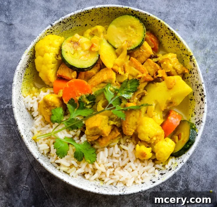 A bowl of rice topped with Easy Tofu and Vegetable Curry featuring crispy tofu pieces, zucchini slices, carrots, and cauliflower. Garnished with fresh cilantro, the dish is presented in a speckled ceramic bowl on a gray textured background.