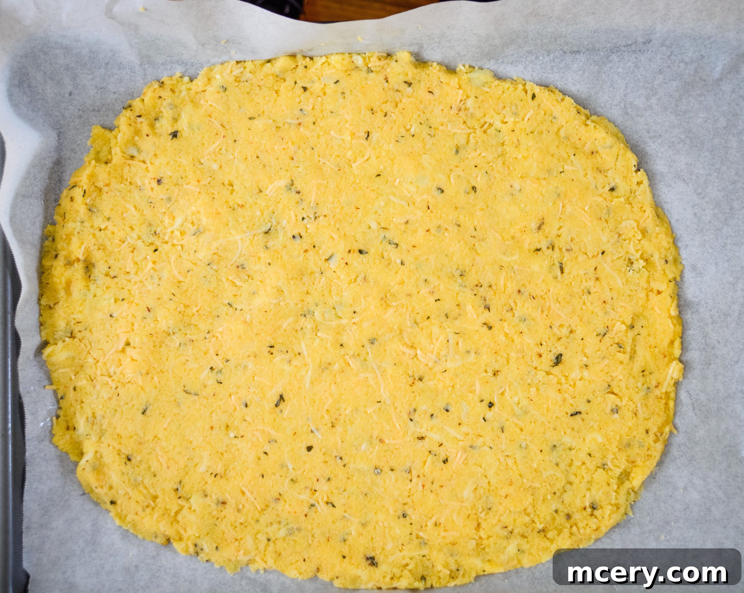 The Ultimate Cauliflower Pizza Base 11 Cauliflower pizza crust shaped on parchment paper on a baking sheet.
