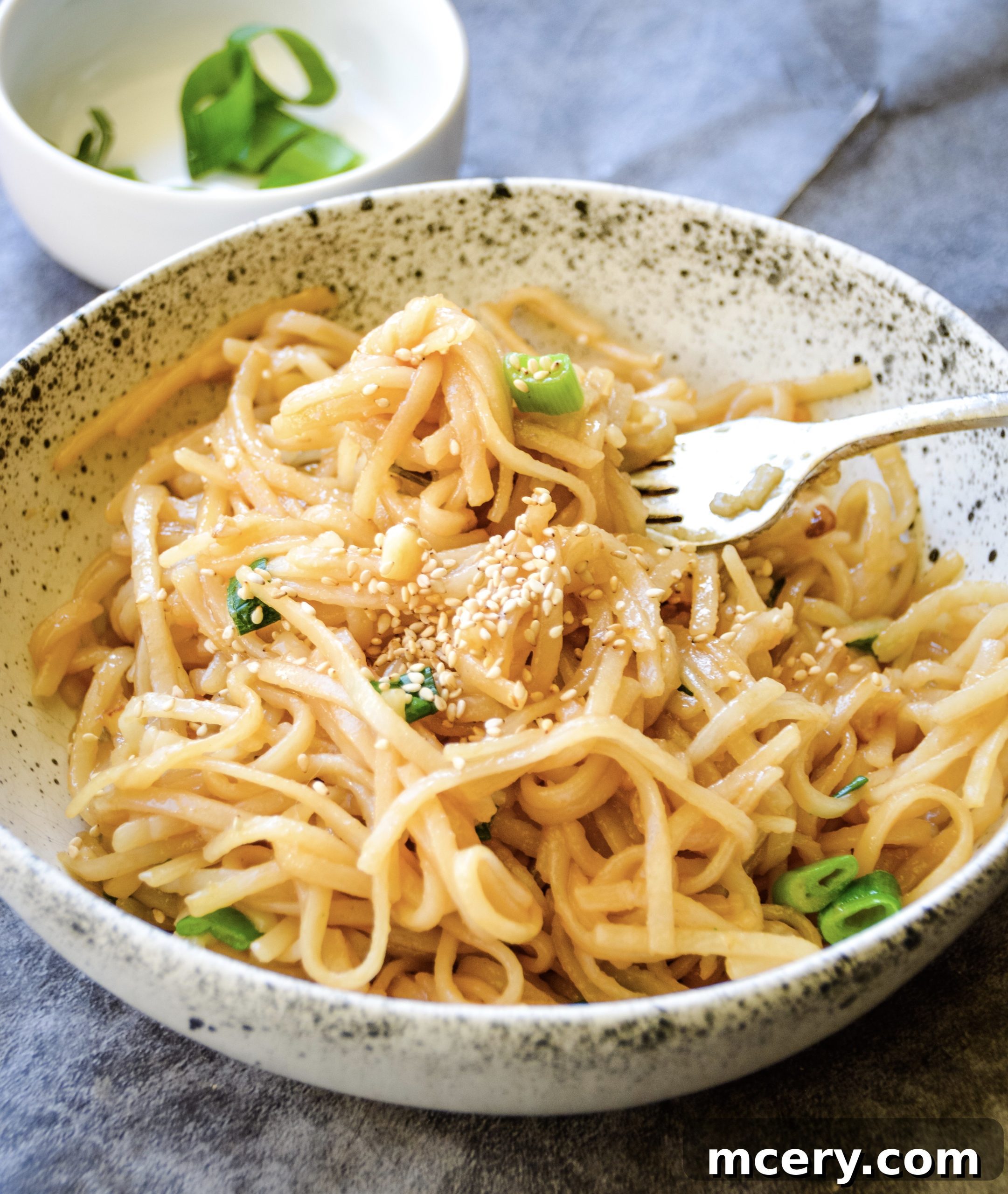 A close-up shot of a bowl of freshly made Asian Garlic Noodles, garnished with chopped green onions and a sprinkle of sesame seeds, ready to be served.