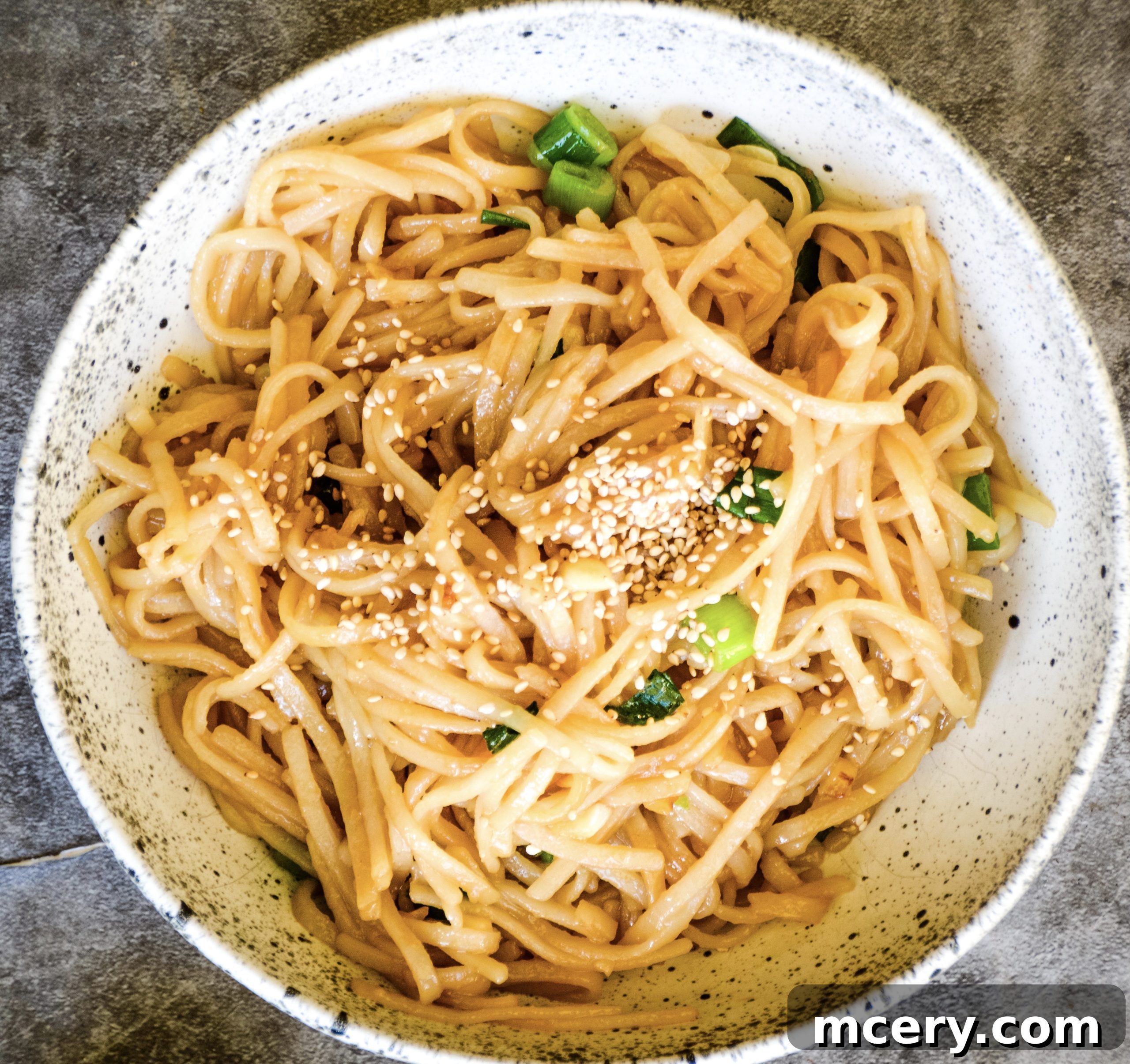 A serving of Asian Garlic Noodles in a bowl, showing the glossy texture of the noodles coated in sauce, garnished with green onions.