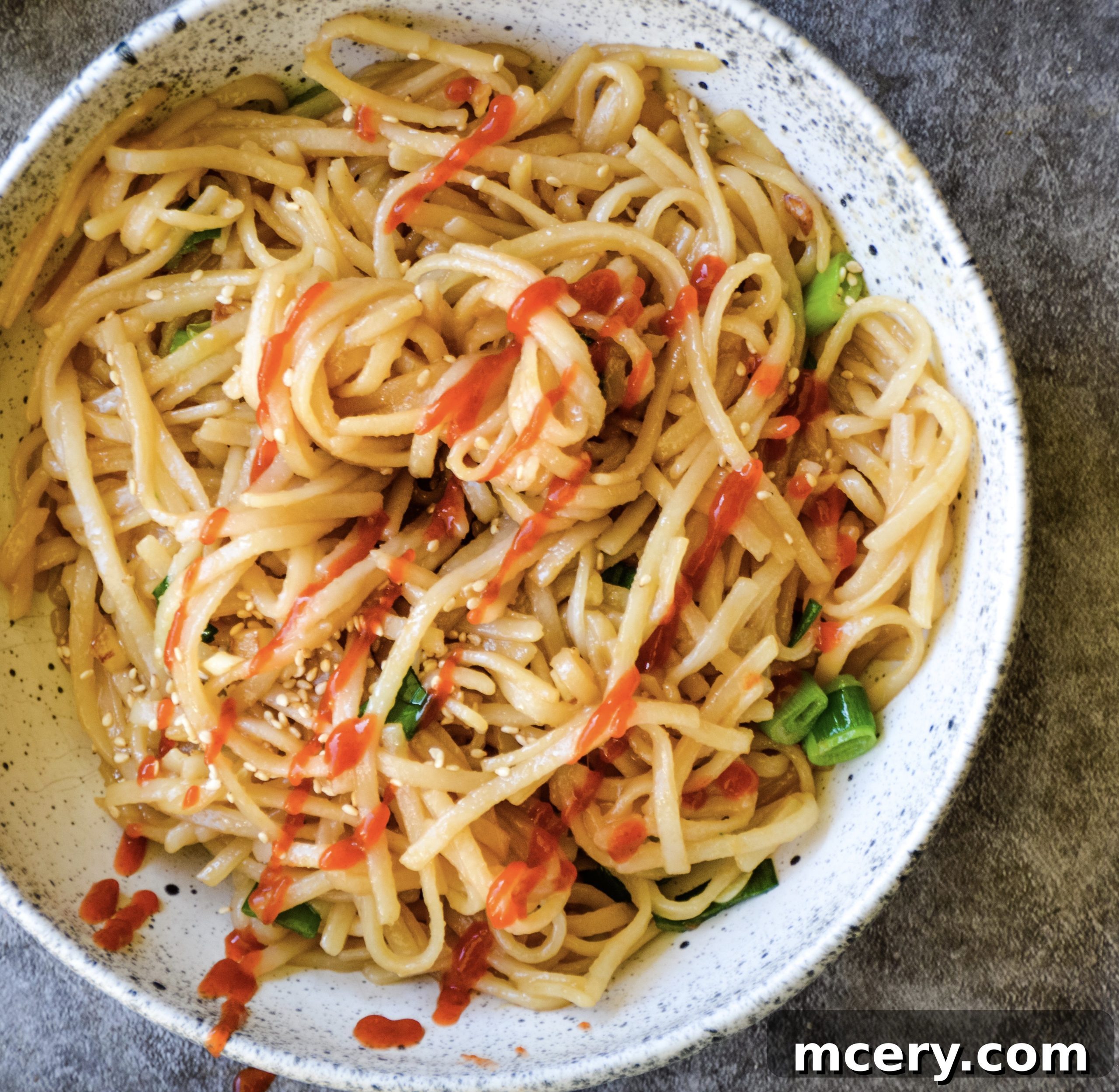 Another angle of Asian Garlic Noodles in a bowl, showcasing the rich sauce and fresh green onion garnish, with chopsticks resting on the side.
