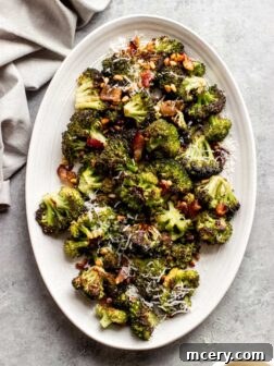 A close-up of the finished roasted broccoli with bacon, pine nuts, and Parmesan in a serving dish, garnished with fresh herbs.