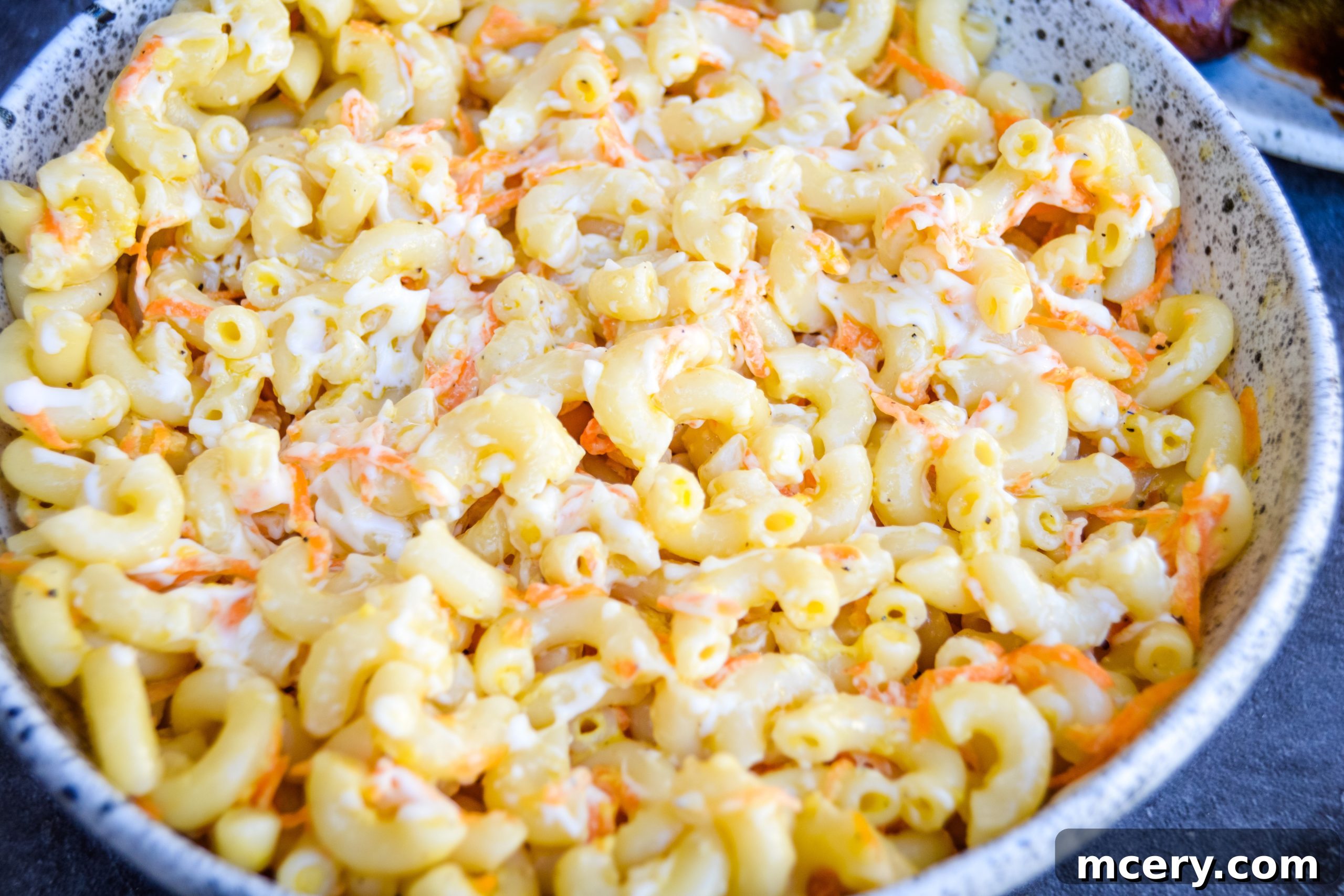 Guilt-Free Hawaiian Macaroni Salad 2 A generous serving of creamy Healthier Hawaiian Macaroni Salad in a rustic white bowl, garnished with a sprig of fresh herbs.
