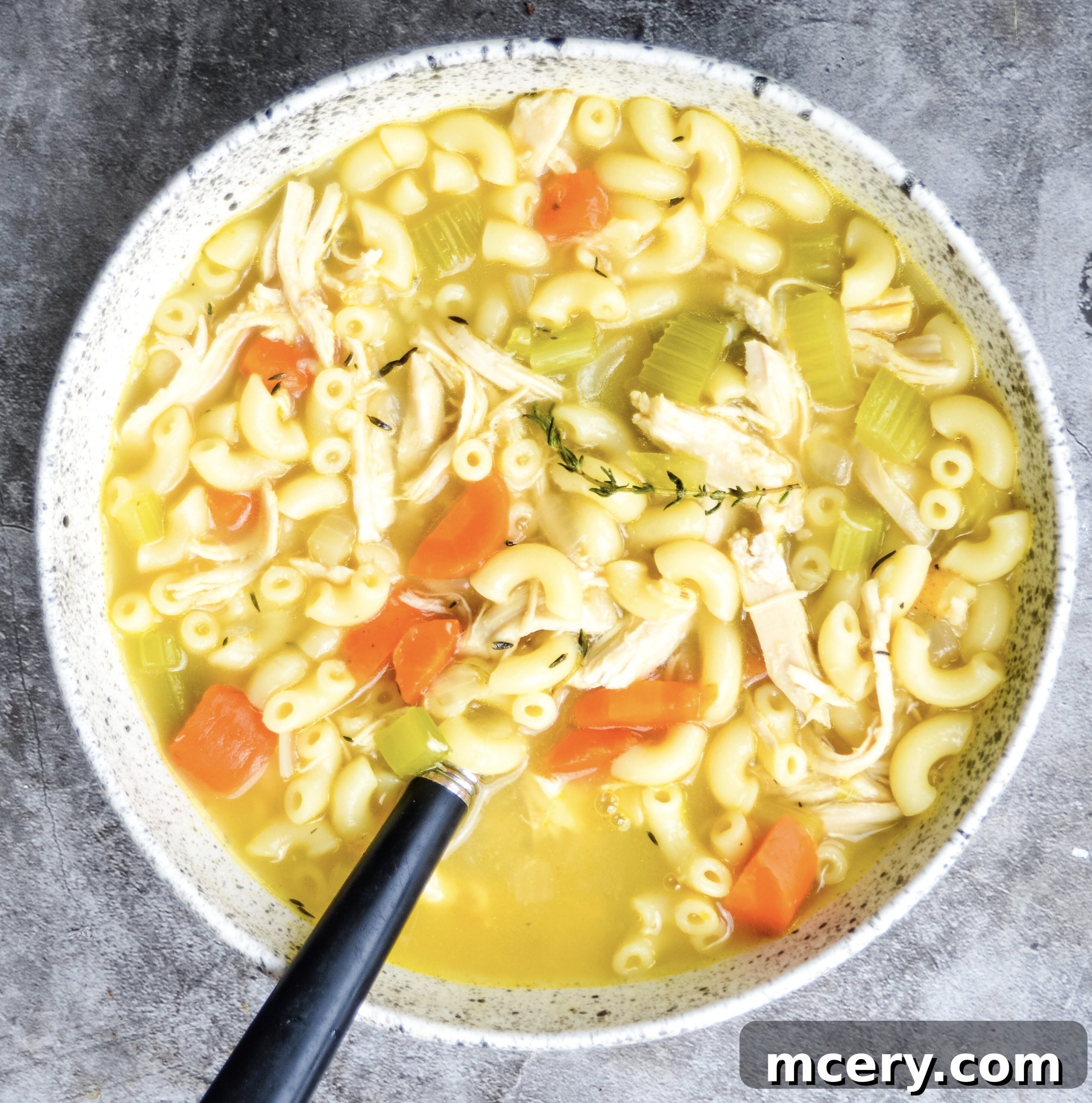 A ladle scooping a generous portion of steaming chicken noodle soup from a large pot into a white serving bowl.