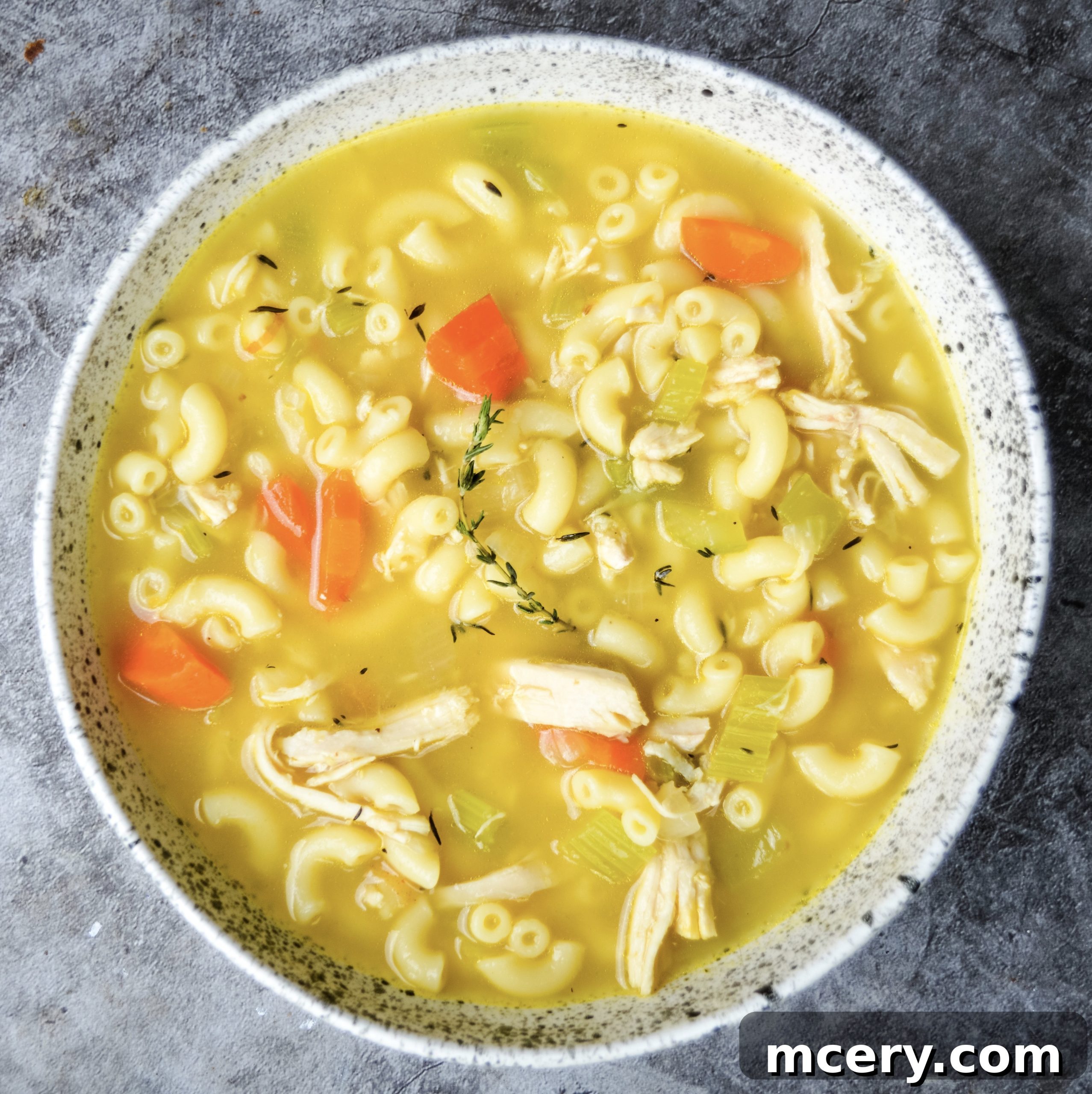 A generous, steaming bowl of chicken noodle soup, with a spoon resting in it, beautifully presented and ready to be enjoyed.