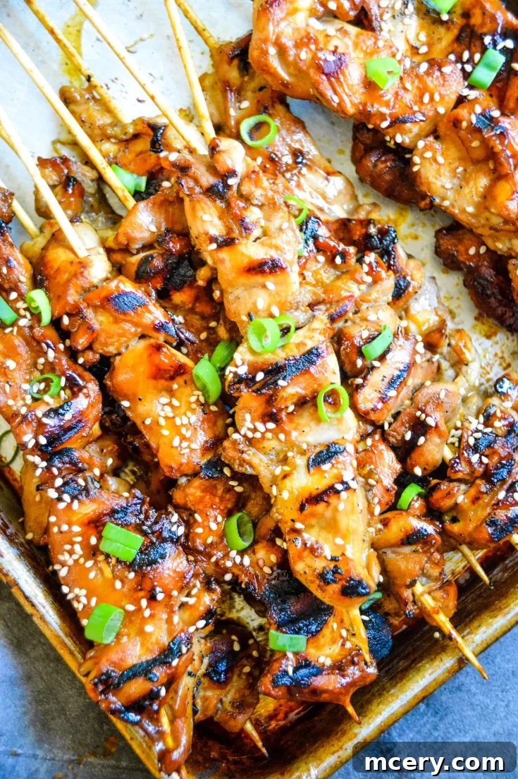 Grilled Teriyaki Chicken Skewers on a baking tray, garnished with sesame seeds and chopped green onions.
